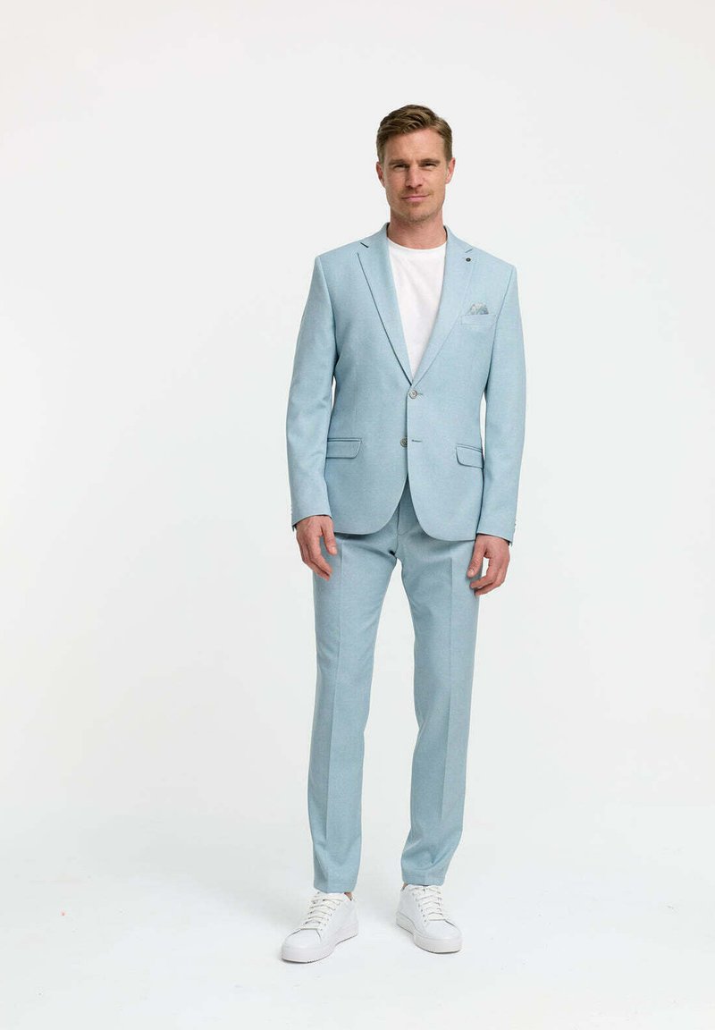 Helles blaues Anzug mit schlanker Passform, Ein-Knopf-Blazer, passenden Hosen und weißen Sneakers. Der Stoff wirkt glatt mit einer strukturierten Detail.