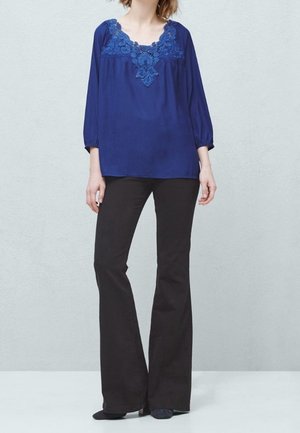 Blusa azul marino con detalles de encaje floral en el escote, combinada con pantalones de campana negros. Tejido suave y corte relajado.