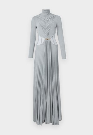 Robe grise longue en tissu élastique. Elle présente un col haut, un buste plissé et une jupe fluide avec une découpe et des détails en métal doré.