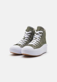 High-top sneakers in olive green canvas with white laces, rubber toe caps, and textured white platform soles. Features contrasting stitching.