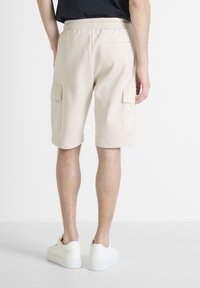 Pantalones cortos beige de carga con cinturilla elástica, dos bolsillos laterales y un bolsillo trasero. Tejido suave con una textura blanda y un corte relajado.
