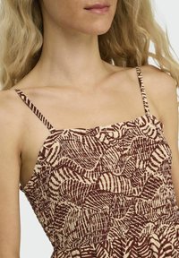 Robe à motifs brun et beige avec de fines bretelles, présentant une texture froncée et des lignes ondulées, créant une apparence en couches.