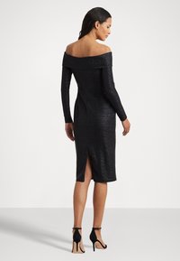 Mustat off-the-shoulder-mekko, jossa on pitkät hihat, teksturoitu kangas, polven mittainen ja sivuaukko; yhdistetty mustiin korkokenkiin.