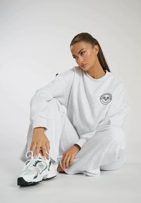 Grijze sweatshirt en sweatpants set met een rond logo, gecombineerd met witte en groene sneakers. Zacht materiaal met een relaxte pasvorm.