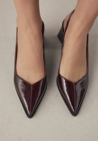Burgundi patentinės odos slingback kulniukai su smailiu nosiu, mažu blokuotu kulnu ir tekstūruotu paviršiumi. Lygus vidus su minimaliais detalėmis.