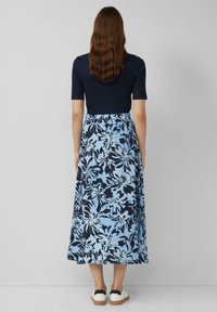 Marineblauwe top met korte mouwen en een rok met blauw bloemenpatroon. De jurk heeft een elastische taille en is enkellang, gecombineerd met witte sneakers.