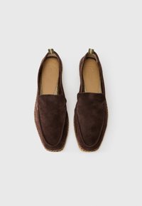 Sötétbarna velúr slip-on loaferek, elasztikus húzófülekkel és látható varrott talppal, fehér háttér előtt.