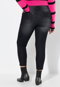 Jeans skinny negros con una cintura de altura media, dos bolsillos traseros y un diseño sin costuras. Combinados con botas de tobillo negras con tachuelas.