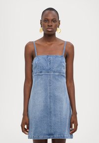 Denimkjole med tynne stropper, lys blå farge, tettsittende liv og utsvingt skjørt. Har sømdetaljer og en rett kanten.