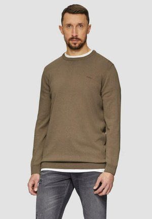 Olivgrüner Rundhalsausschnittpullover mit gerippten Manschetten und Saum, versehen mit einem dezenten Logo auf der Brust. Kombiniert mit hellgrauen, destroyed Jeans.