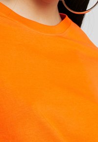Camiseta de algodón naranja brillante con cuello redondo, mangas cortas y textura suave. Costuras visibles en el cuello, mostrando un diseño casual.