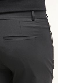 Schwarze Hose mit einer glatten, matten Textur, einer dezenten Tasche auf der Rückseite und einem silbernen Reißverschluss an der Seite für den Verschluss.