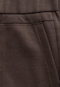 Bruin textiel met een gridpatroon, met een subtiele glans en gestikte details; inclusief een zak voor functionaliteit.