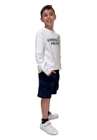 Camicia bianca a maniche lunghe con la scritta "AERONAUTIC MILITARY", pantaloni cargo blu scuro e sneakers bianche con dettagli rossi e calzini neri.