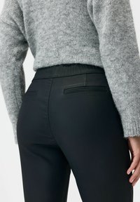 Czarne dopasowane spodnie o gładkiej fakturze, z elastycznym pasem i dwoma tylnymi kieszeniami. Połączone z szarym, teksturowanym swetrem.