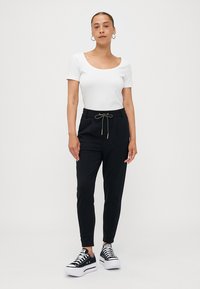 Pantalons de jogging noirs avec une taille à cordon, coupe slim et poches latérales, associés à un t-shirt blanc ajusté et des baskets noires.