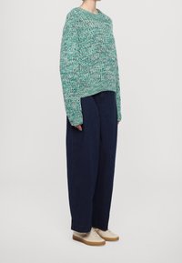 Gestrickter Pullover in Türkis mit lockerer Passform und weiten Ärmeln, kombiniert mit navyblauen Baggy-Hosen und beigen Schnürschuhen.