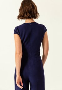 Námořnický overal s krátkými rukávy, přiléhavý střih, zadní zip a detail pasu na míru. Hladká látka se strukturovanou siluetou.