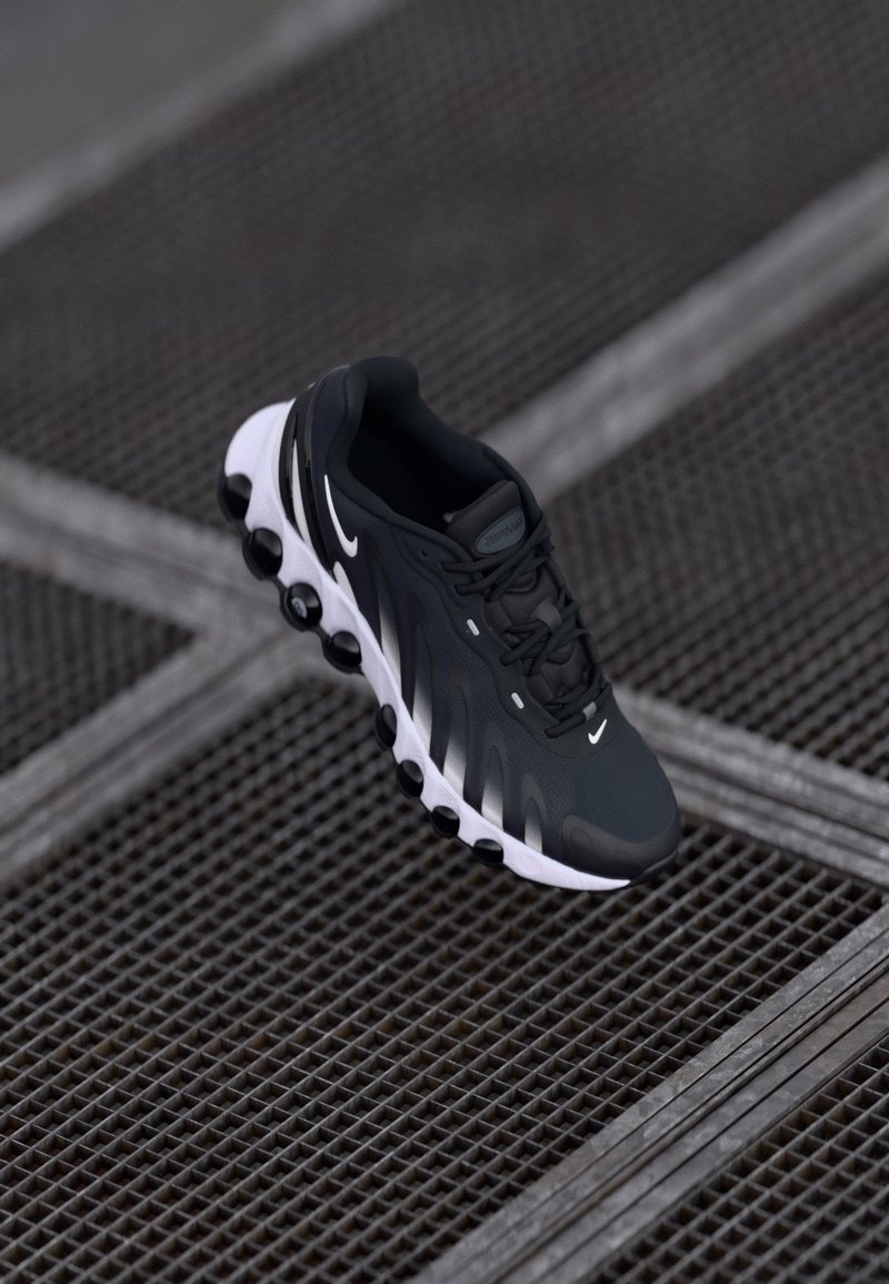 Zwarte sportieve schoen met witte accenten, bovenwerk van mesh en gestructureerd ontwerp. Beschikt over een ronde zool met pods voor demping en grip.