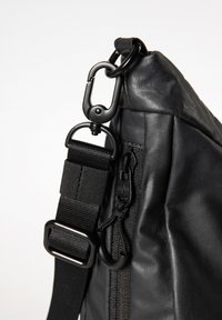 Zwarte, getextureerde, waterbestendige tas met een afneembare schouderband, metalen hardware en ritsdetails. Beschikt over een stevige clip en een verstelbare strap.