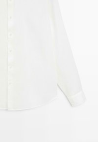 Chemise blanche à manches longues à boutons, avec un ourlet arrondi et des poignets boutonnés, vue de face et recadrée à la taille.