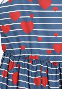 Modré šaty s bílými pruhy a červenými srdíčkovými vzory, s nařasenou sukní a hladkým materiálem.