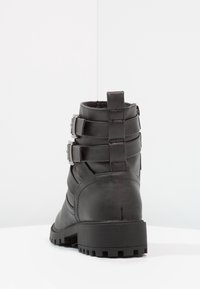 Botín negro de cuero hasta el tobillo con paneles texturizados, hebillas de metal ajustables y una suela de goma con un patrón de tracción.