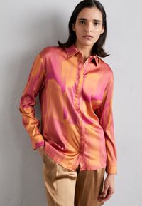 Satinbluse i livlig rosa- og oransje-gradient, med knappestilling foran, lange ermer og en strukturert krage med en glatt tekstur.