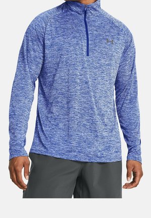 Mężczyzna w niebieskim, teksturowanym sportowym pulowerze z długim rękawem, z zamkiem do ćwierci długości i małym logo na piersi.
