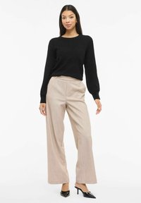 Must tekstuuriga kampsun pikkade varrukatega, kombineeritud beežide kõrge vöökohaga laiade pükstega ja mustade teravate varvastega kontsadega.