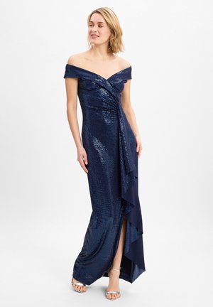 Abito in sequins blu navy con scollatura a spalle scoperte, dettagli drappeggiati e un'apertura laterale. Texture liscia con accenti a strati all'orlo.