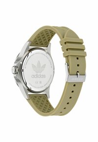 Ezüst színű rozsdamentes acél óra világos olajzöld gumiszíjjal, melynek texturált mintázata van. Az óra hátulján Adidas logó található.