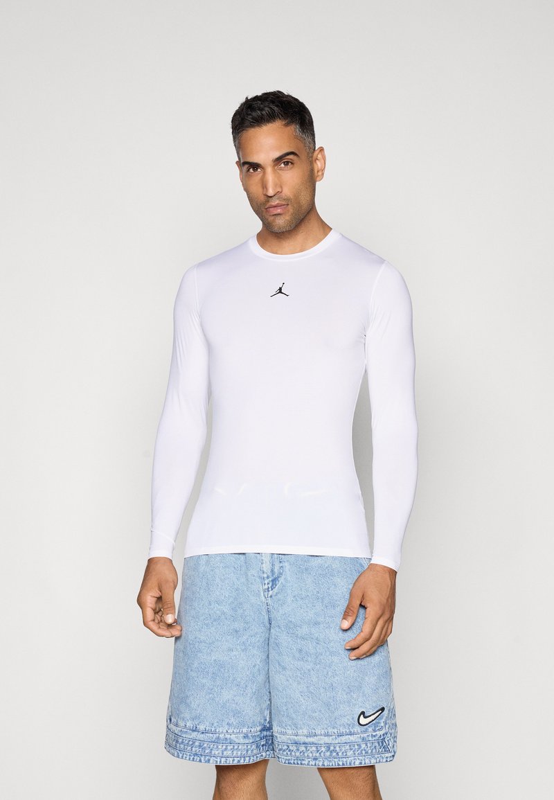 Langærmet fitted hvid sports skjorte med et sort Jumpman logo, parret med lyse denim shorts med en sort Nike swoosh.