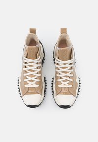 Sneakers sznurowane z błyszczącą, beżową cholewką z białymi akcentami, teksturowaną czarną podeszwą oraz wyściełanym kostką dla wsparcia.