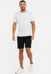 T-shirt en coton blanc, col ras du cou, associé à un short noir retroussé et des baskets blanches. Design simple, sans logos ni motifs visibles.