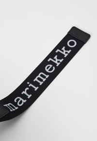 Cintura in tessuto nero con la scritta "marimekko" in bold lettere bianche. La texture è intrecciata con una finitura liscia, terminando con un pezzo d'accento nero.
