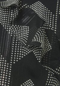 Schwarzer Stoff mit weißen Punkten und geometrischen Mustern, mit strukturiertem Oberflächen und geschichteten Rüschendetails entlang des Randes.