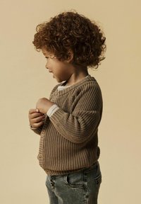 Brauner Strickcardigan mit geripptem Muster, graue Jeans und schichtetes, weiß-grau gestreiftes Hemd, seitlich gezeigt.