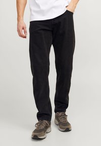 Black cotton trousers with a relaxed fit, featuring side pockets and visible stitching. Worn with gray sneakers.
