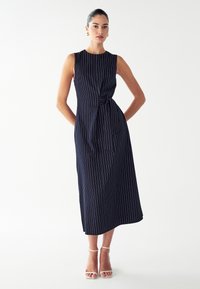 Mouwloze marineblauwe jurk met witte pinstrepen, geknoopte taille-informatie en een midi-lengte. Glad materiaal met een ontspannen silhouet.