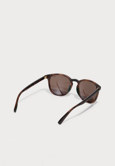 Ochelari de soare tortoiseshell maro, cu lentile rotunde, brațe subțiri și accente verzi pe partea interioară. Prezintă un logo subtil.