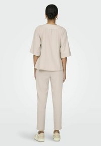 Beige linnen twee-delige outfit met een losse top met korte mouwen en tapse broek, gecombineerd met lichtgekleurde sneakers. Zachte textuur, casual ontwerp.