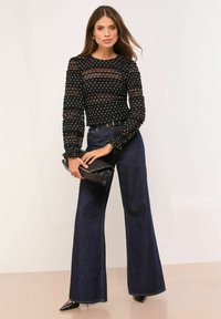 Mustvalge täpilise musta pika varrukaga top, millel on läbipaistvad detailid, sobitatud tumelõviliste laia säärtega teksade ja musta käekotiga. Teravad kontsad lõpetavad välimuse.