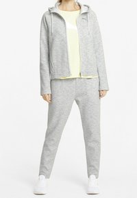 Sudadera de forro polar gris con cremallera y pantalones de chándal, combinados con una camiseta corta amarilla. Presenta un corte relajado y detalles en zapatillas blancas.