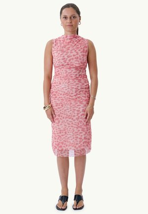 Jeune femme debout de face portant une robe rose sans manches à imprimé animalier et des sandales noires à bout ouvert avec des bracelets.