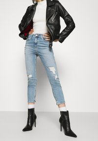 Chaqueta de moto de cuero negra con cremallera plateada, camiseta blanca de canalé, jeans de tiro alto desgastados en azul claro y botines negros de punta.