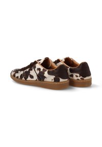 Zapatillas de gamuza con estampado de vaca que presentan acentos marrones, una silueta baja y una suela de goma con detalles de costura visibles en los bordes.