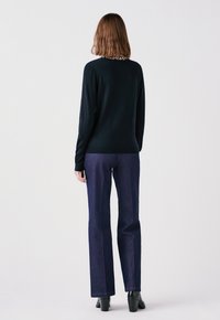 Maglione nero a maniche lunghe con colletto a stampa leopardata, abbinato a jeans dritti blu scuro e stivaletti neri con tacco.