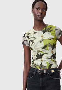 T-shirt med korte ærmer med blomstermotiv; prydet med store hvide blomster på en grøn baggrund og en tætsiddende pasform. Bæres med sorte jeans.