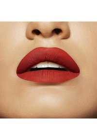 Rouge à lèvres mat rouge sur des lèvres pulpeuses avec une texture lisse, mettant en valeur une couleur audacieuse contre un teint clair. Légère brillance sur les dents.